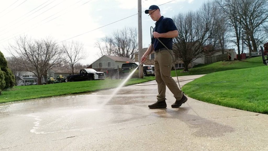 A Big Wave Window service technician pressure washing a concrete driveway