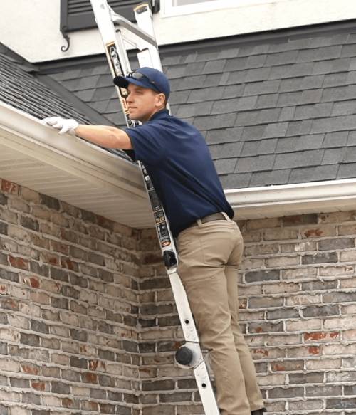 A Big Wave Window service technician cleaning gutters while on a ladder